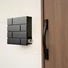 A black mailbox with a newspaper tube is mounted on a white wall next to a wooden door with a black handle. Voir les images du produit