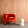 An orange armchair and a cream side table are placed in front of a wooden wall and on a speckled floor. Anteprima dell’immagine prodotto