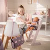A young girl is playing with a doll in a high chair at a small table, with a bed in the background. Náhľad obrázku produktu