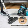 A vacuum cleaner on a white rug, with a person's legs in the background. A close-up inset shows the vacuum head on a wooden floor. Produktbild-Vorschau