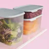 Two clear plastic food storage containers with gray lids, one filled with salad and the other with sliced cantaloupe and cherry tomatoes, are placed on a white surface against a pink background. Produktbild-Vorschau