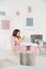 A young girl sits on a pink child's sofa, looking at something in her hands. The room is decorated with framed art on the wall. Voir les images du produit