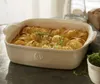 A close-up shot of a baked potato dish in a ceramic baking dish, with a loaf of bread and a glass in the background. Produktbild-Vorschau