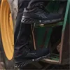 A person wearing black work pants and black safety shoes is stepping onto the green metal steps of a tractor. A yellow tractor wheel is visible on the left. Náhľad obrázku produktu