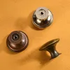 Three cabinet knobs of different styles and finishes are placed on an orange textured surface. Produktbild-Vorschau