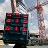 A person carrying a stack of Metabo toolboxes on a construction site with a crane in the background. Produktbild-Vorschau