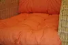 A close-up view of an orange cushion on a wicker chair. Produktbild-Vorschau