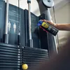 A hand holding a spray can near a weight machine in a gym. Podgląd zdjęcia produktu