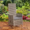 A polyrattan garden chair with a gray cushion is placed on a wooden deck in a lush garden with colorful flowers and greenery. Produktbild-Vorschau