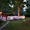 An outdoor garden party setting with string lights, tables, chairs, and people mingling. Anteprima dell’immagine prodotto