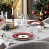 A festive Christmas table setting with plates, glasses, a candle, and a Christmas tree in the background. Voir les images du produit