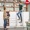 A couple is in a kitchen, with the man on a step ladder reaching for something on a shelf and the woman holding books. Náhled obrázku produktu