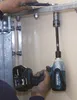 A person is using a power tool to tighten a bolt on a metal fixture attached to a wall. Podgląd zdjęcia produktu