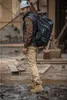 A man wearing work clothes and a hard hat stands in a construction site, carrying a large backpack. Produktbild-Vorschau