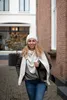 A woman wearing a hat and scarf walks down a cobblestone street. Produktbild-Vorschau