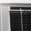 A close-up view of black aluminum blinds installed in a white window frame. Produktbild-Vorschau