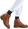 A pair of brown leather boots worn by a person wearing light-wash jeans and black socks. Produktbild-Vorschau