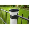 A close-up of a black metal fence with a white post and a black solar light on top. The background shows a green lawn and some potted plants. Voir les images du produit