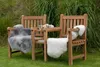 Two wooden chairs with sheepskin throws in a garden setting. Produktbild-Vorschau
