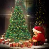 A baby dressed as Santa Claus sits next to a decorated Christmas tree, holding a teddy bear. Produktbild-Vorschau