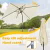 An outdoor scene with a cream-colored rectangular umbrella open, and a folded umbrella to the right. The background shows trees and a hillside under a blue sky with clouds. Text overlays highlight features. Produktbild-Vorschau