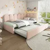 A child's bedroom with a pink upholstered daybed and trundle bed pulled out, decorated with playful wall art and string lights. Náhled obrázku produktu