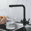 A hand is holding a glass pitcher under a black faucet in a kitchen sink, filling it with water. Produktbild-Vorschau