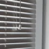 A close-up view of silver-colored blinds with a pull cord and tassel. Produktbild-Vorschau