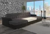 A spacious living room with a large U-shaped sofa, a floor lamp, and a view of a city skyline through a large window. Produktbild-Vorschau
