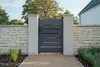 A modern gray aluminum garden gate is shown in an outdoor setting, flanked by stone walls and white pillars, with landscaping in the foreground and background. Produktbild-Vorschau
