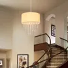 A modern chandelier with a fabric shade and crystal accents hangs in a grand entryway with a curved staircase. Náhľad obrázku produktu