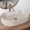 A beige matte washbasin with a gold faucet is placed on a wooden countertop, with a round mirror reflecting the faucet and basin in the background. Produktbild-Vorschau