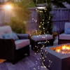 A solar-powered string light hanging in a backyard patio setting with chairs and a fire pit. Voir les images du produit