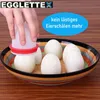 A hand is using a silicone egg peeler to remove the shell from a hard-boiled egg, which is placed in a decorative bowl with other peeled eggs. Produktbild-Vorschau