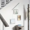 A set of hanging picture frames displayed on a wall next to a staircase and a coat rack. Podgląd zdjęcia produktu