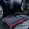 A red and black mechanic's creeper is positioned in front of a dark blue car in a garage setting. Tools and equipment are visible in the background. Voir les images du produit