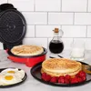 A breakfast scene featuring a waffle maker, waffles, fried eggs, raspberries, syrup, and milk. Podgląd zdjęcia produktu