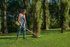 A woman is using a string trimmer in a garden with trees. Produktbild-Vorschau