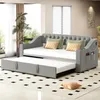 A grey sofa bed with a pull-out trundle bed is shown in a living room setting. Produktbild-Vorschau