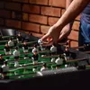 A person's hands are holding a foosball, about to place it on a foosball table with miniature players. Náhled obrázku produktu