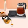 A hand is pouring tea from a teapot into a cup, with an electric kettle on a heating base in the background. Podgląd zdjęcia produktu