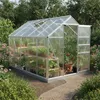A greenhouse filled with plants and gardening supplies, set in a garden with flowers and trees. Produktbild-Vorschau