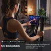 A woman is using a home elliptical trainer while looking at a tablet screen displaying a workout video. Produktbild-Vorschau