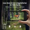 A hand holding a smartphone displaying a live feed from a trail camera in a forest setting. The trail camera itself is visible in the foreground. Produktbild-Vorschau