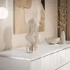 A close-up view of a white dresser with decorative items on top, including a bust, a bowl, and a vase with dried foliage. Produktbild-Vorschau