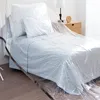A bed covered with a clear plastic tarp, with a bedside table and lamp in the background. Produktbild-Vorschau