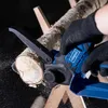A person wearing black gloves is using a blue and black cordless chainsaw to cut a log that is supported by a wooden stand. Voir les images du produit