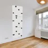 A white climbing wall with black grips is mounted vertically on a white wall in a room with wooden flooring and a window. Anteprima dell’immagine prodotto