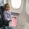 A young girl sits on an airplane seat with a blanket and a pig-shaped pillow. Produktbild-Vorschau