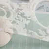 A close-up view of a white, ornate fabric trim with text visible on a light blue background. Produktbild-Vorschau